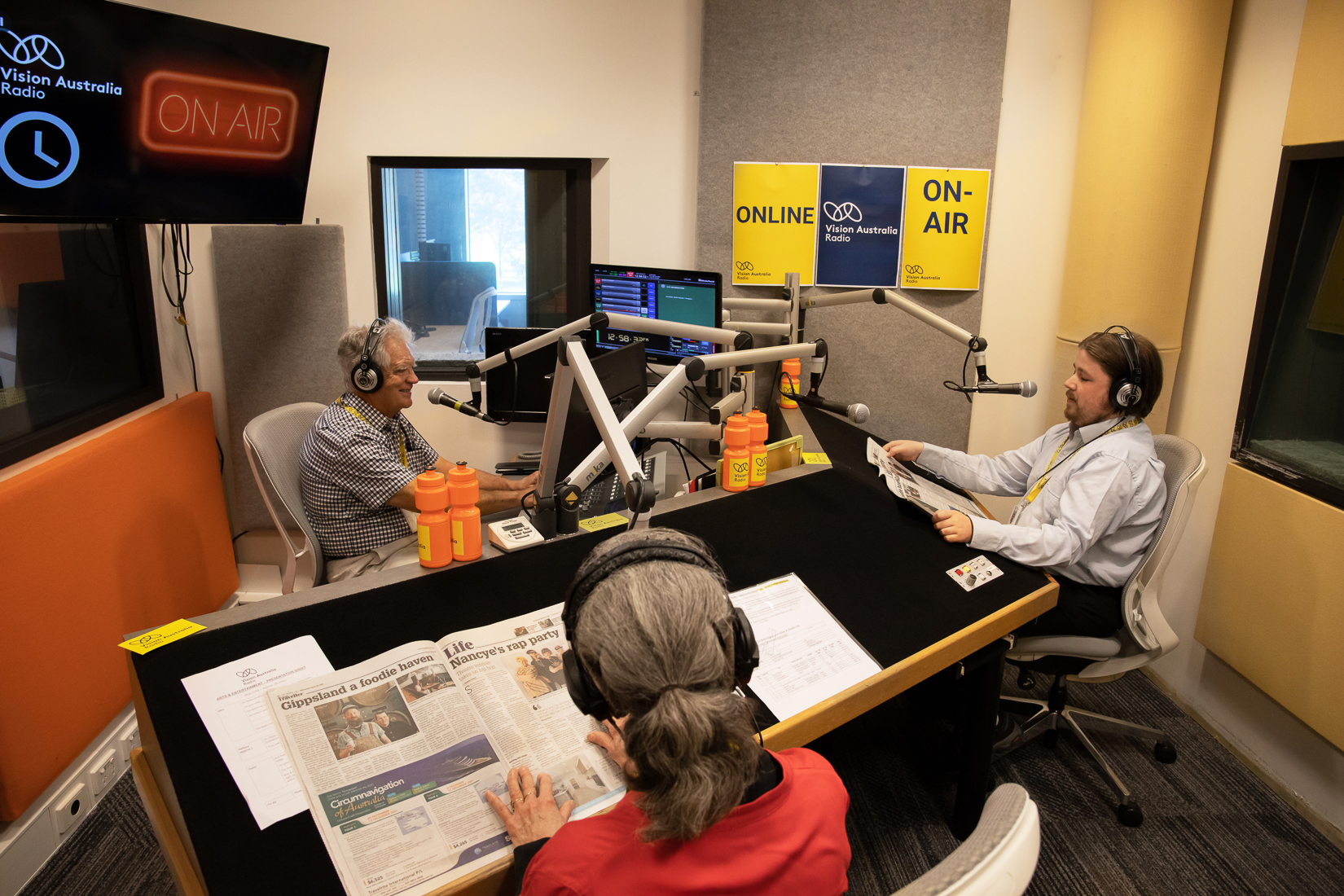 Two men and a woman sit in a radio studio