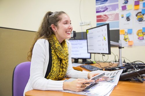 A young woman sits at a desk and holds a handheld magnifier