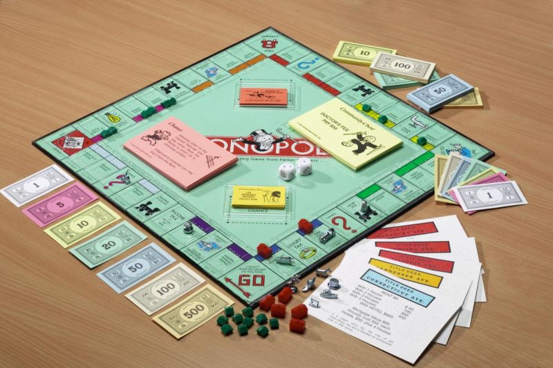 A green 51cm square braille Monopoly board, complete with play money, playing cards, green and red houses and a pair of dice.