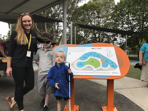 A woman stands next to two young children in front of a sign in a playground