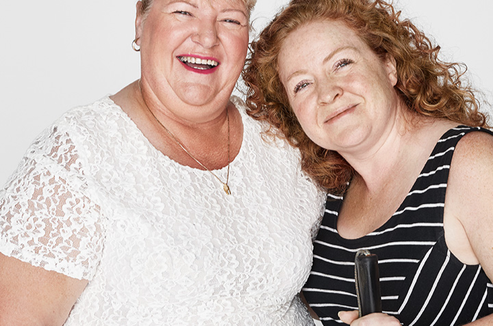 Vision Australia clients Debra and Sarah smiling at camera. Sarah is holding a cane.