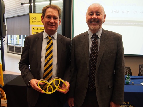 "Two men in suits, one holds a trophy in the shape of the Vision Australia logo"