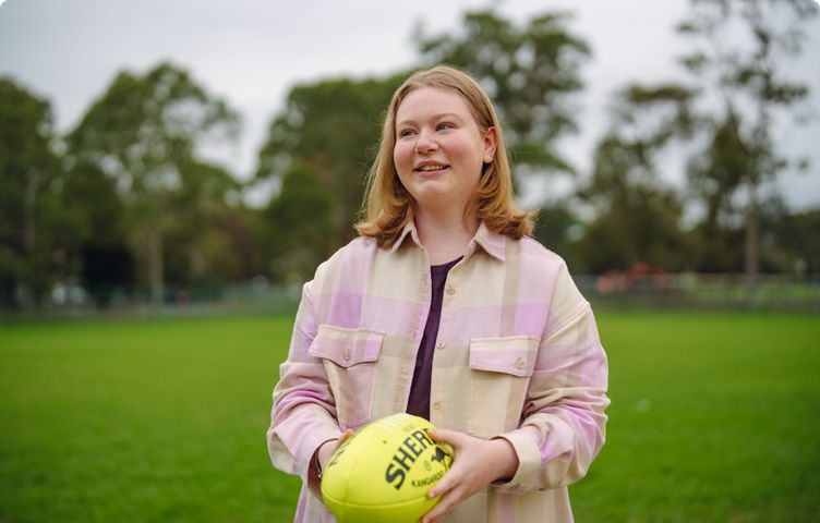A girl is standing in an oval and is holding a yellow football.