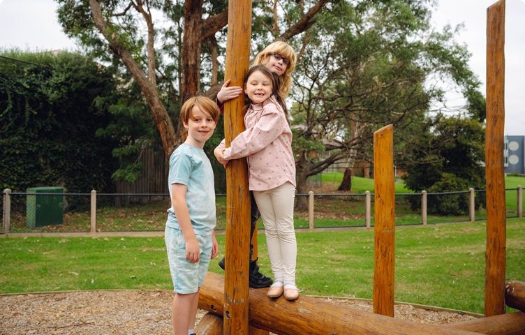 Three children happily posing beside a playground pole.