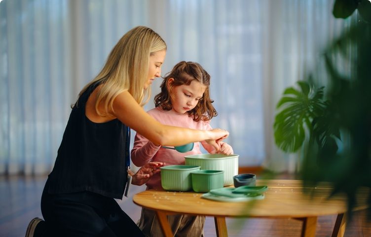 A Vision Australia team member and a girl are using scoops and containers at a table.