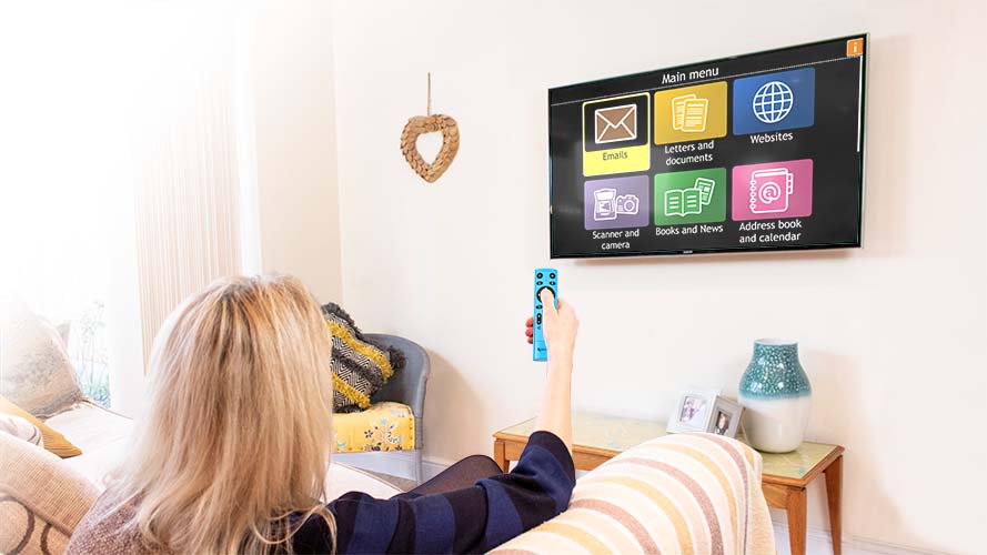 Dolphin GuideConnect software running on a large screen TV, mounted to a wall. A woman is sitting on a couch controlling the TV with the GuideConnect remote