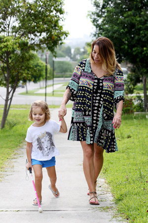 Kaylah walks along the footpath with her mum, holding hands. Kaylah is using her pink cane.