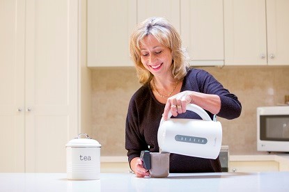 A women stands in a kitchen pouring water from a kettle into a mug with a liquid level attached