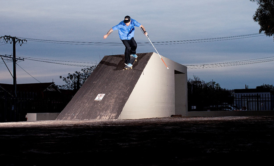 Richard skating down the bunker with his cane. He is wearing a black hat, blue shirt, and black pants. His cane is in his left hand.