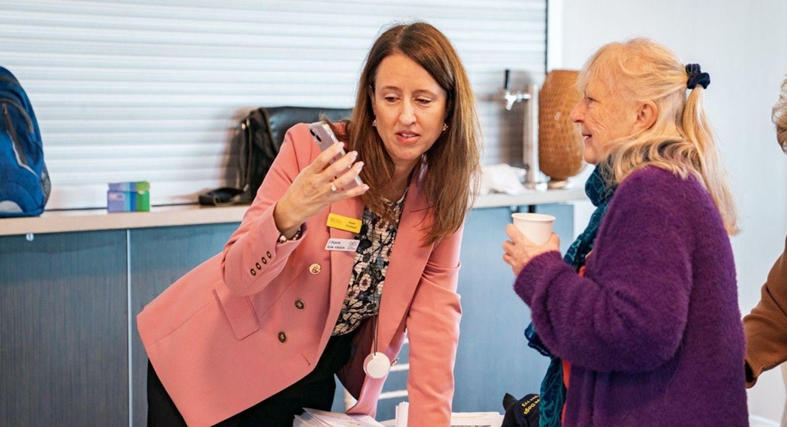 Karen is talking to another woman and they are looking towards her phone.