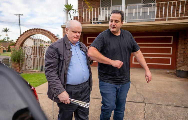 A rideshare driver guides a passenger holding a white cane to a vehicle