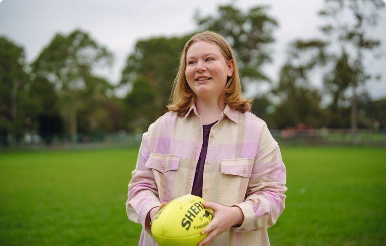 A girl is standing in an oval and is holding a yellow football.