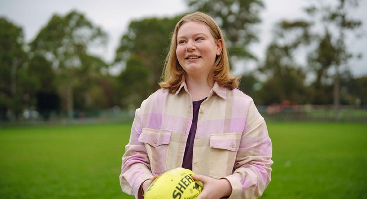 A girl is standing in an oval and is holding a yellow football