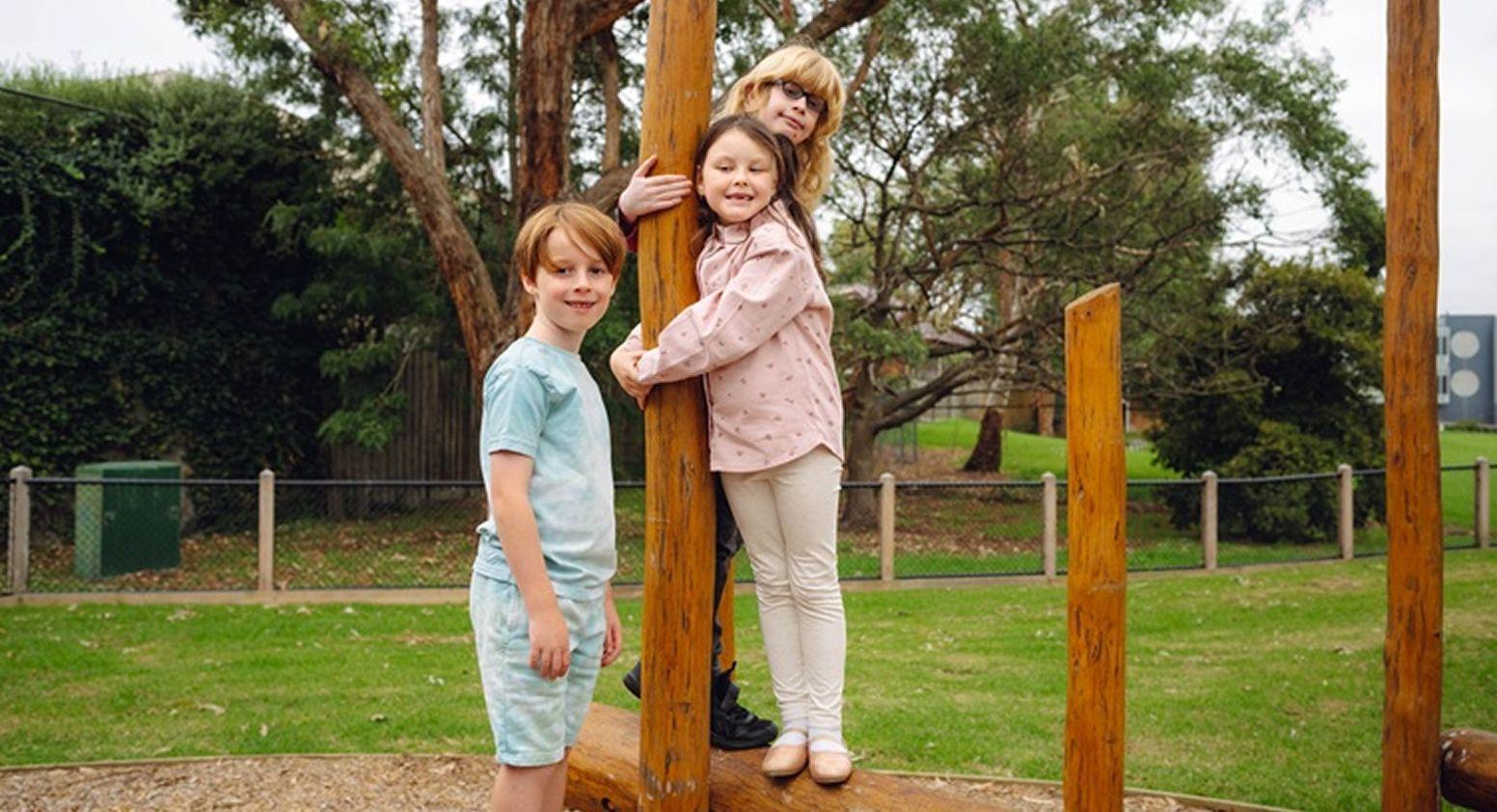 Three children happily posing beside a playground pole.