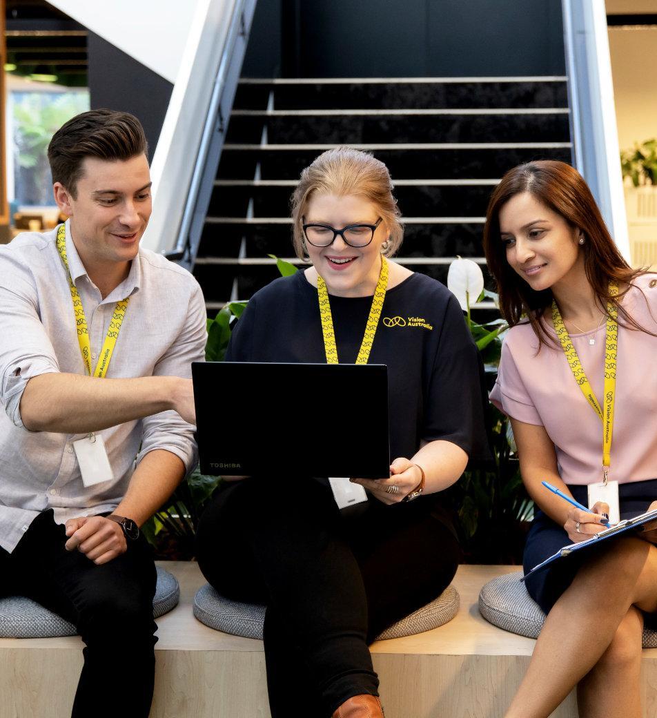 Three work colleagues gathered around a laptop, looking at the screen.