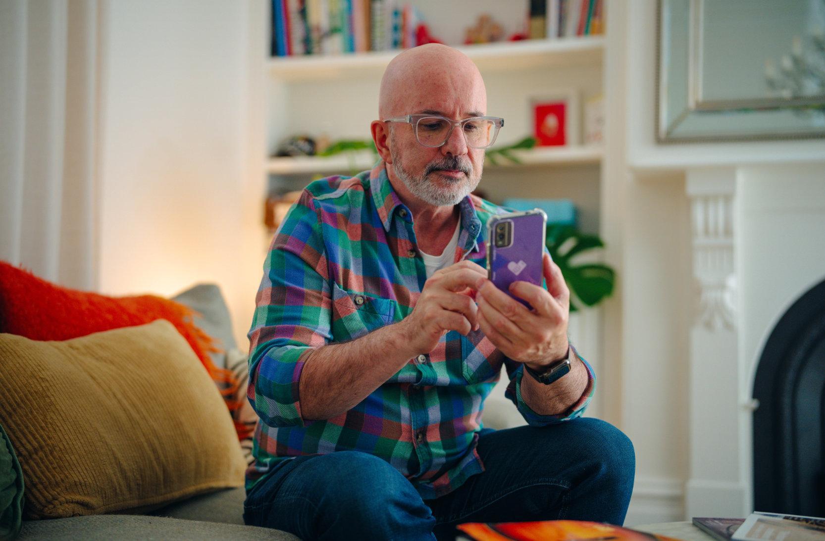 A man is sitting on his couch, scrolling on his mobile phone