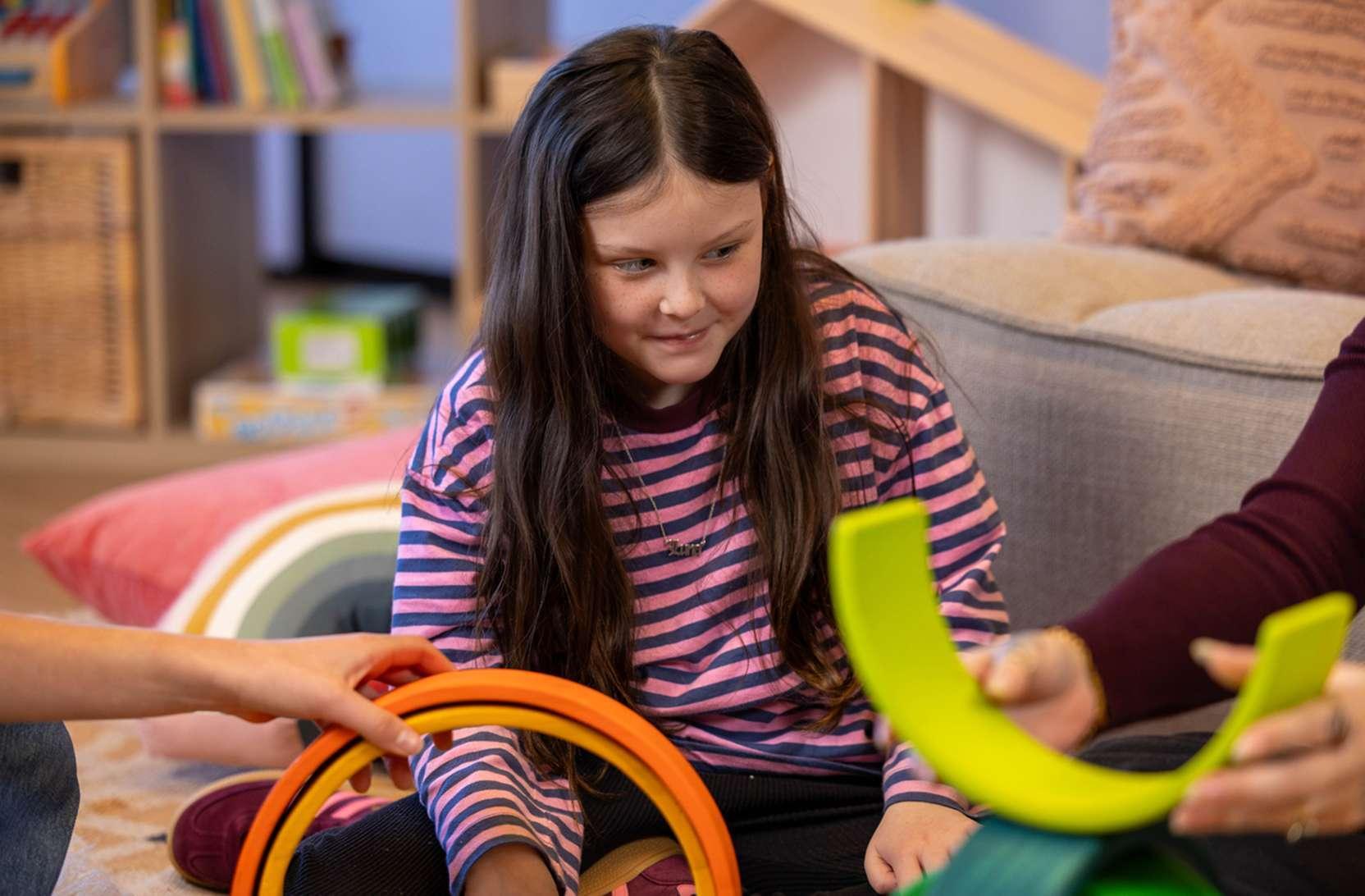 A young girl who has low vision smiles, enjoying an accessible puzzle game with her mum and her primary service provider.