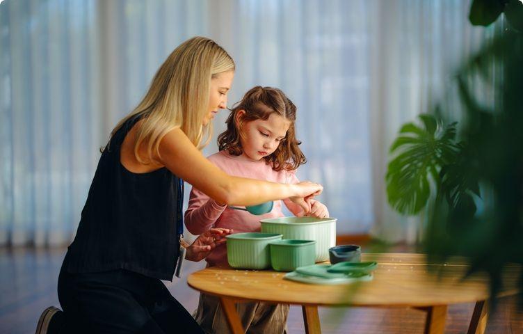 A Vision Australia team member and a girl are using scoops and containers at a table.