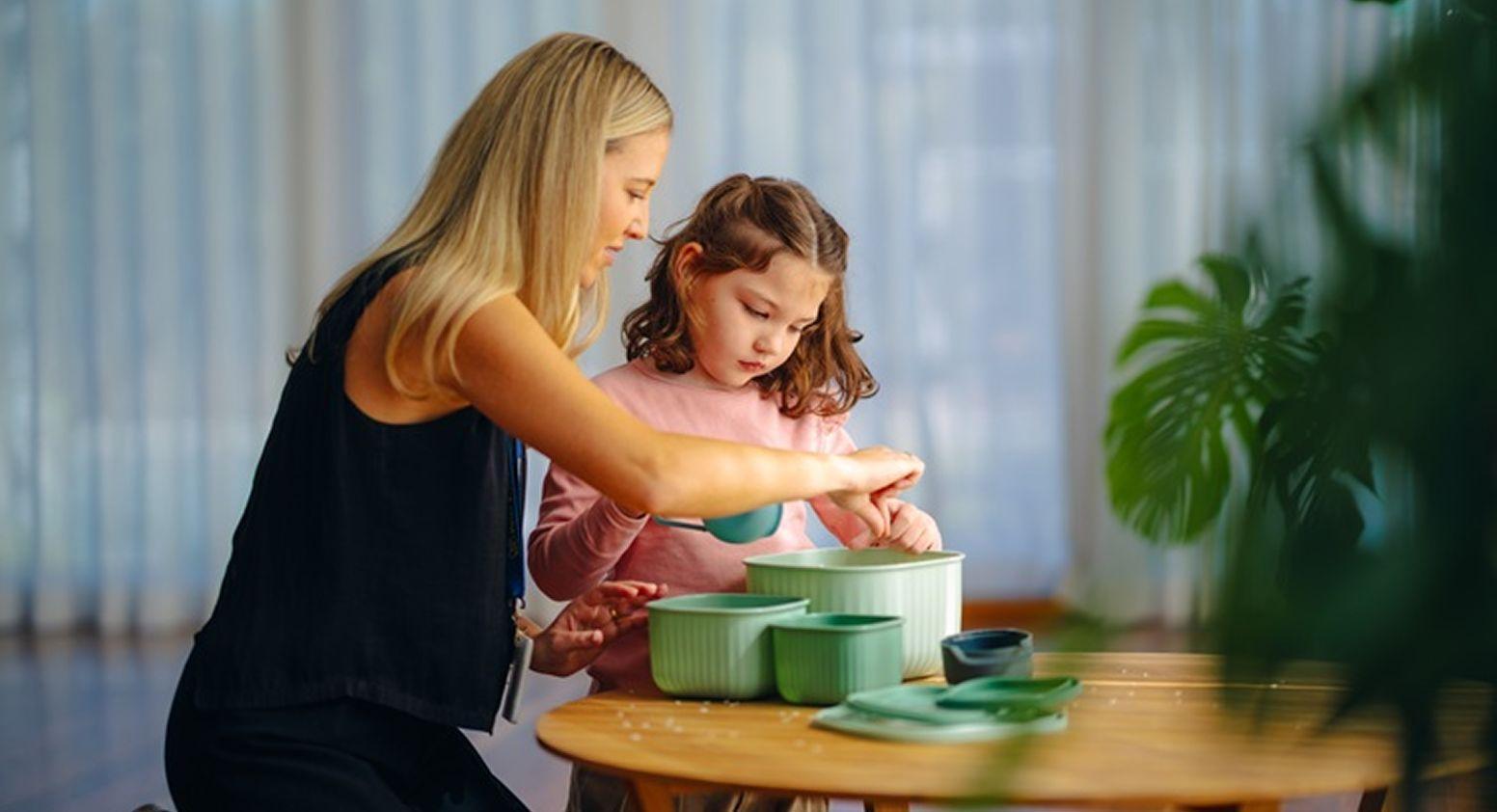 A Vision Australia team member and a girl are using scoops and containers at a table.
